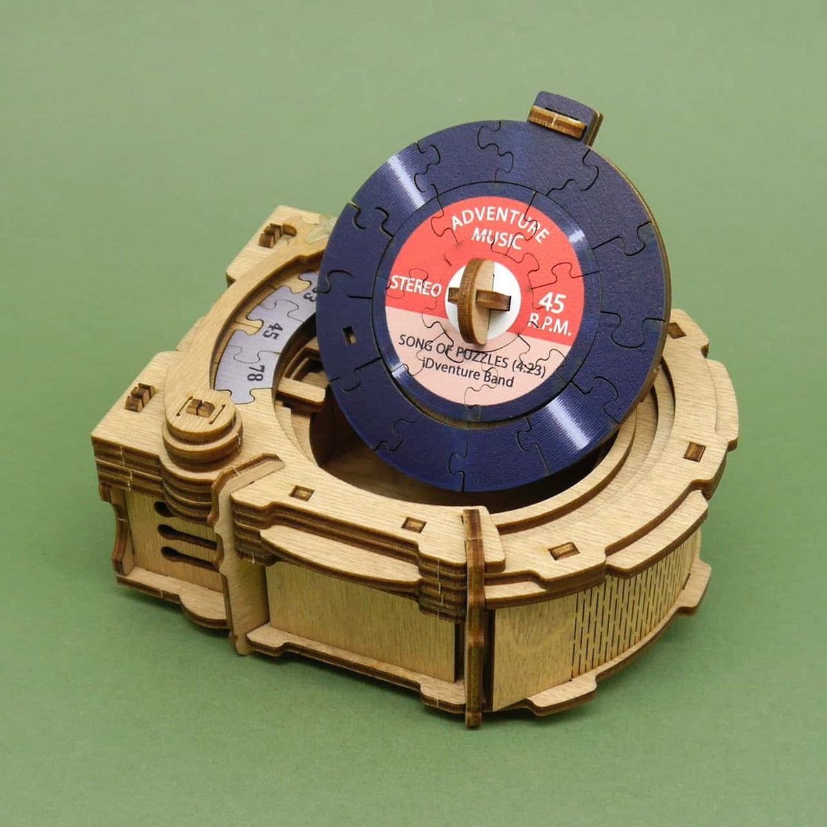 Schräg fotografierte Schachtel des Cluepuzzle Record Player Logikpuzzle vor grünem Hintergrund, Verpackung zeigt Modell und Einzelteile.