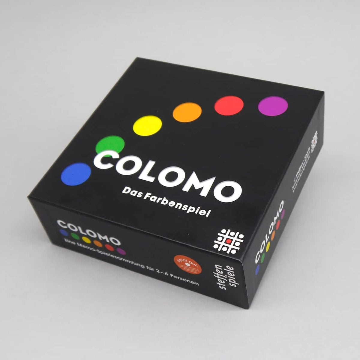 Schwarze COLOMO-Box des Farbenspiels mit halbkreisförmig angeordneten bunten Punkten auf grauem Hintergrund.