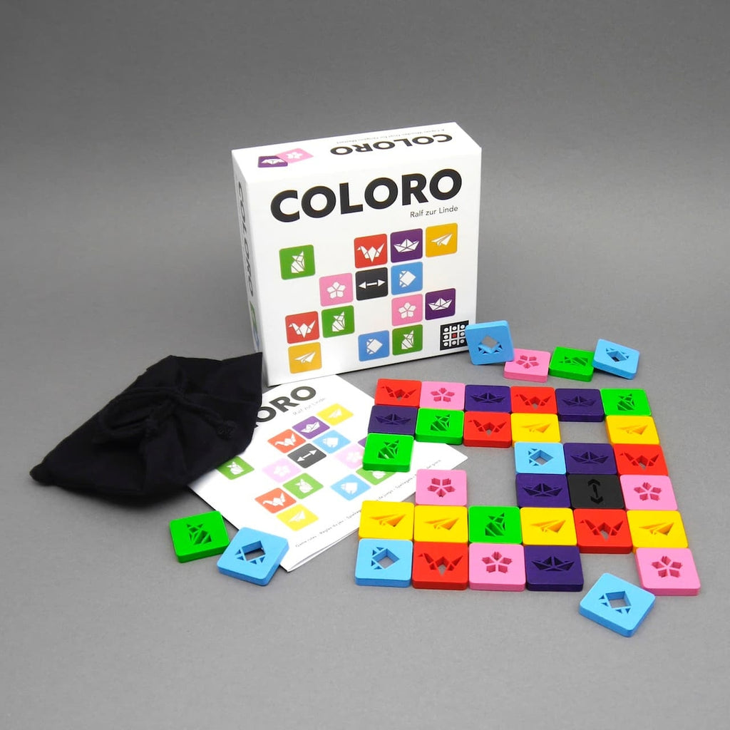 Holzspiel Coloro mit Spielschachtel, Anleitung, schwarzem Beutel und ausgelegten bunten Steinen auf grauer Fläche.