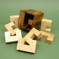 Zerlegte Holzstücke eines 3D-Puzzles liegen vor einer geöffneten Würfelbox auf grünem Hintergrund.