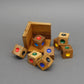 Zerlegtes Geduldspiel aus Holzwürfeln mit bunten Farbpunkten, verteilt vor einer offenen Holzbox auf grauem Untergrund.