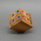 Schräg balancierender Holzwürfel-Knobelpuzzle mit abwechselnden roten und blauen Punktmarkierungen vor neutralem Grau.