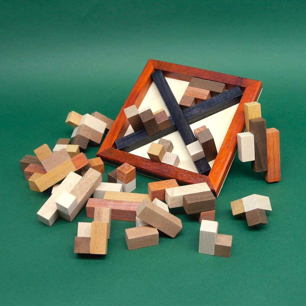 Teilweise zerlegtes Denkspiel mit verstreuten Bausteinen und einem leeren quadratischen Rahmen mit diagonalen Trennleisten.
