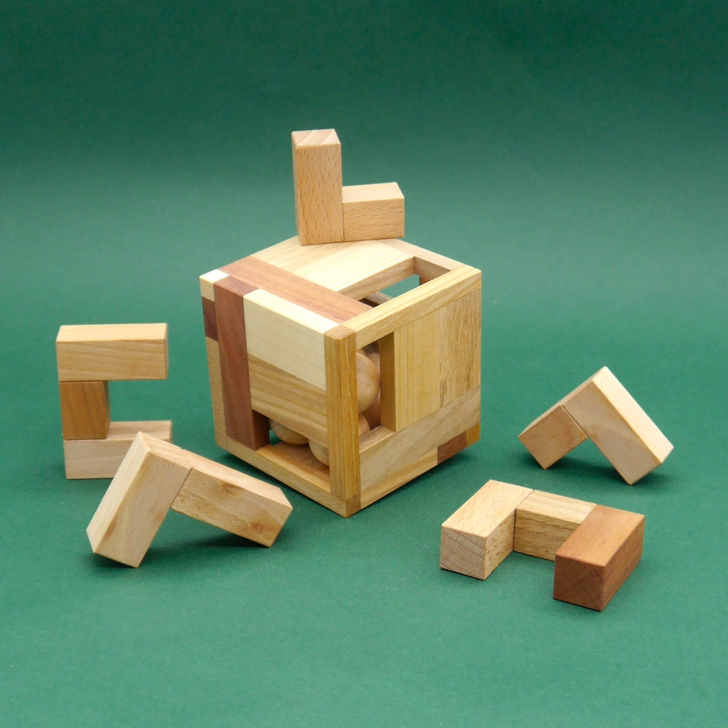 Cubell Holzpuzzle: offener Holzwürfel mit sichtbaren Kugeln im Inneren, umgeben von fünf L-förmigen Holzteilen.