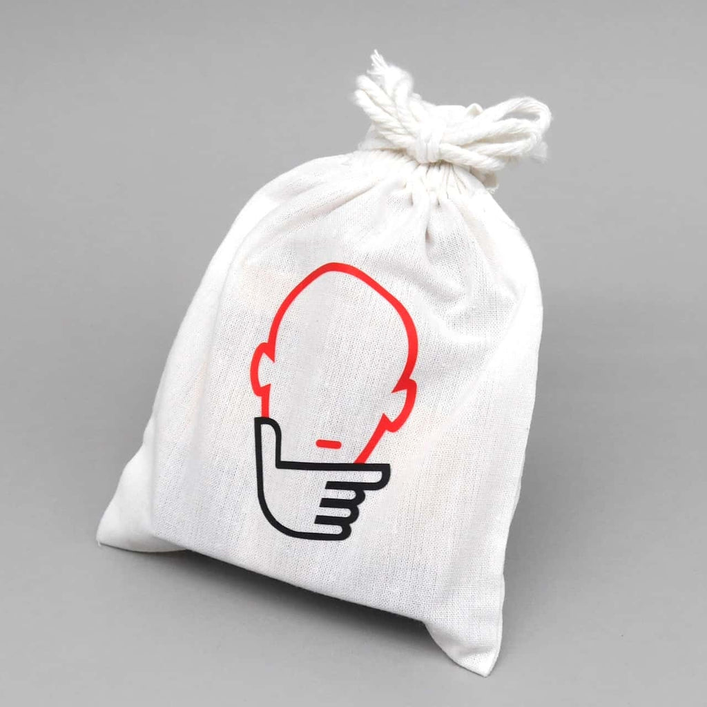Ein cremeweißer Stoffbeutel mit rot-schwarzem Kopf-und-Hand-Logo enthält einen kompakten Brainteaser für geduldige Knobelfreunde.