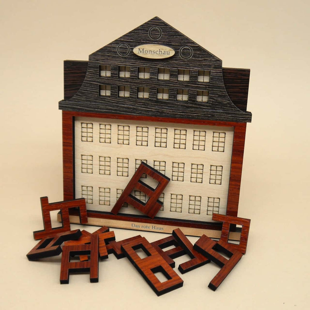 Holzpuzzle ‚Das rote Haus‘: Mehrere unterschiedlich geformte Holzteile und ein rotes Hauptelement, die zusammen ein Haus ergeben sollen.