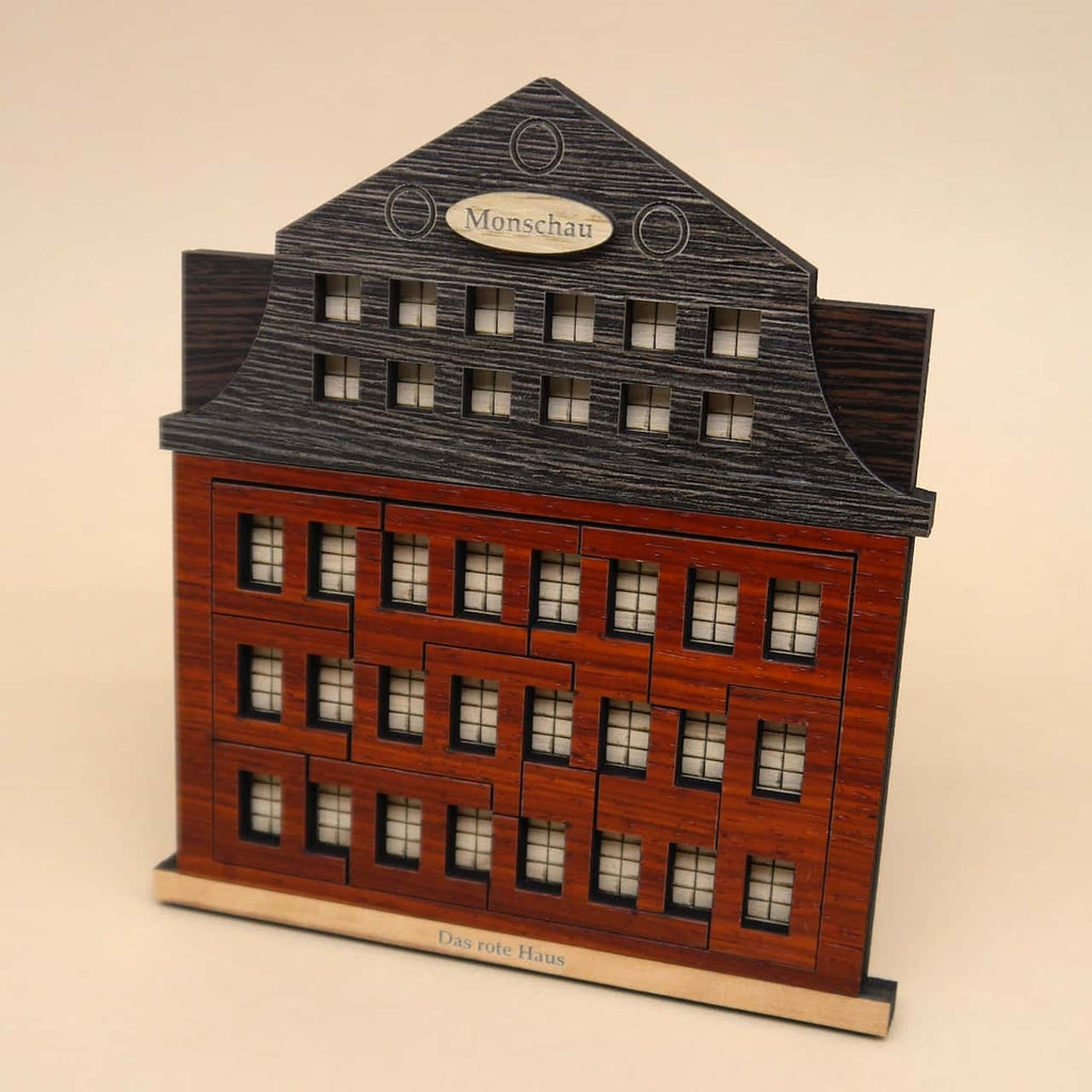 Komplett zusammengesetztes ‚Das rote Haus‘-Holzpuzzle: Alle Teile fügen sich zu einem roten Haus mit hölzernem Fundament und Seitenwänden zusammen.