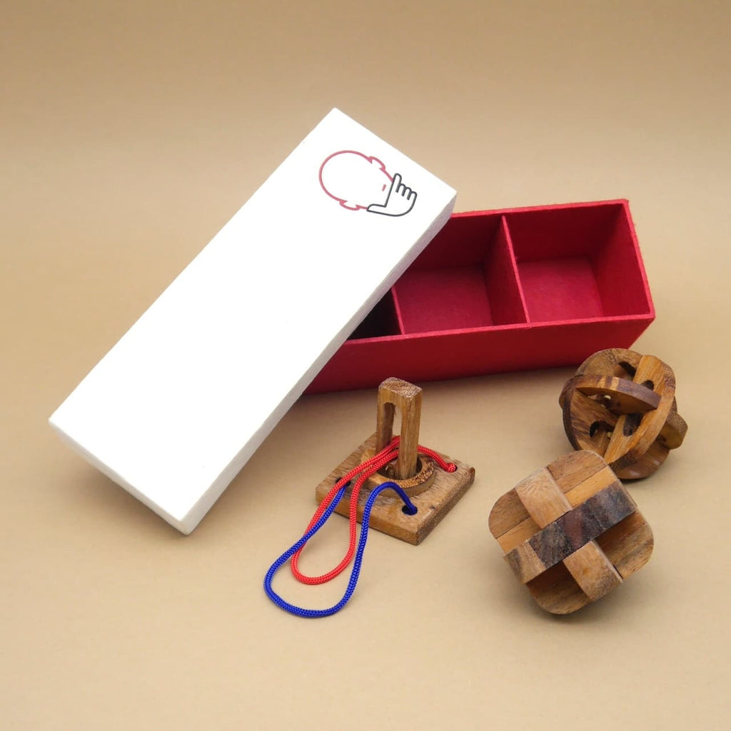 Ein geöffnetes Geschenkset mit drei Knobelspielen aus Holz, inklusive roter Geschenkbox mit Fächern auf neutralem Hintergrund.
