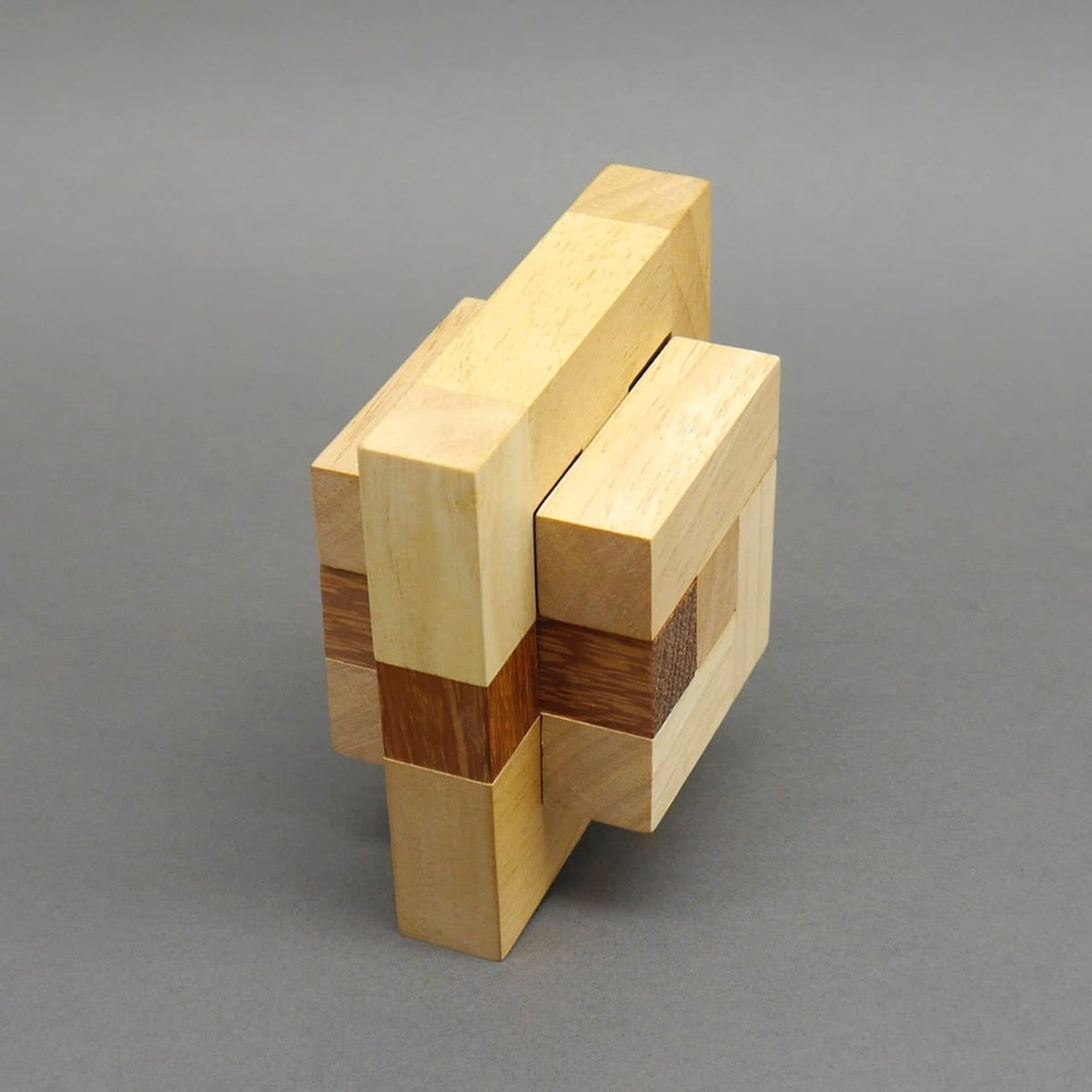 Ein komplett zusammengesetztes Holz‑Geduldspiel aus verschachtelten Quadern steht aufrecht vor neutral grauem Hintergrund.