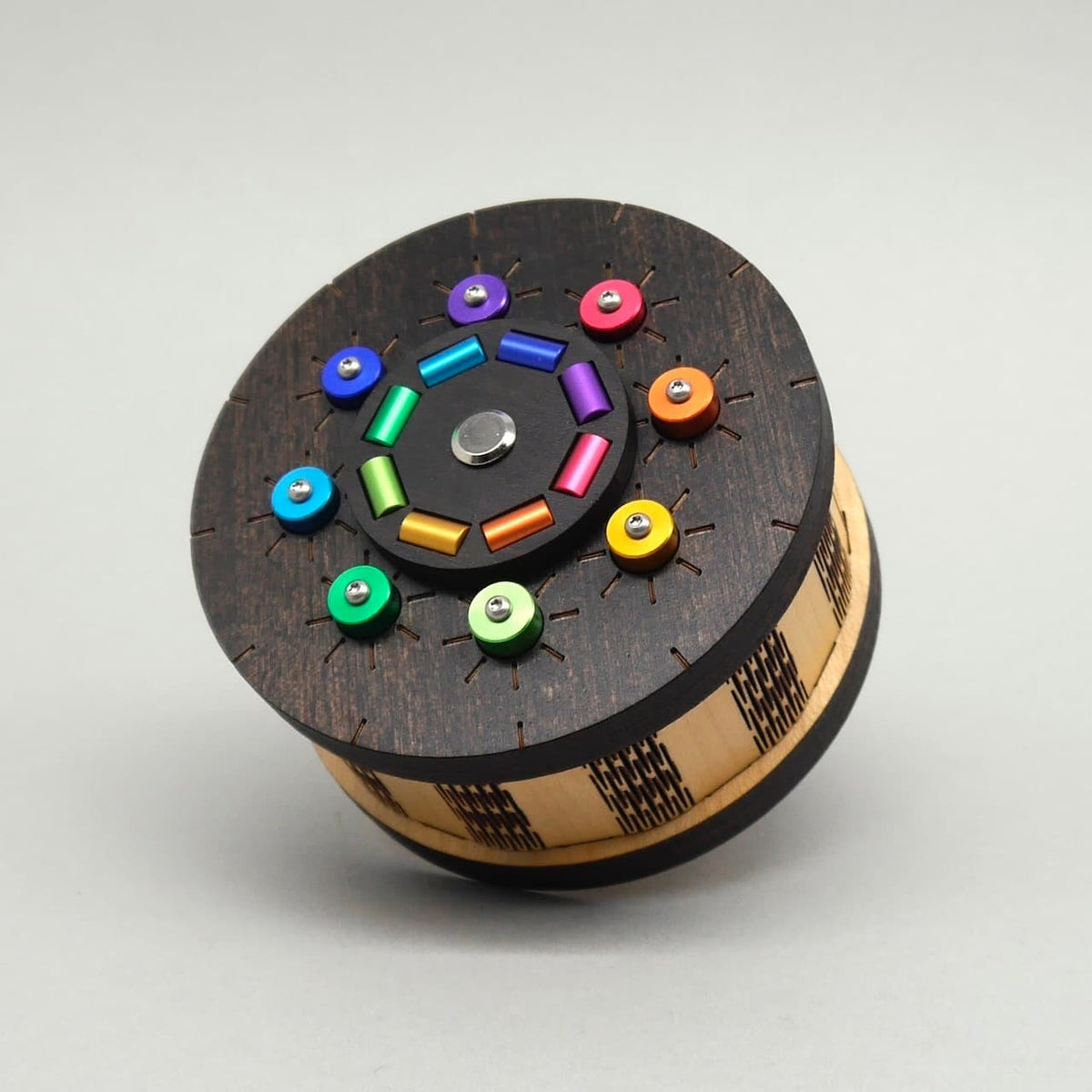 Runde Holzbox mit dekorativem Deckel, verziert mit farbigen Metallknöpfen und gravierten Mustern – geeignet als Denkspiel oder Geschenkverpackung.