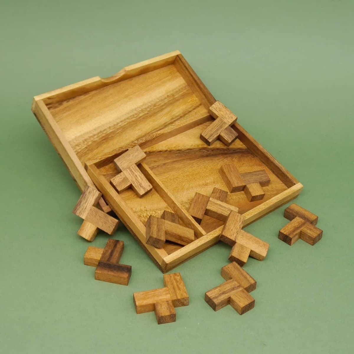 Offenes Holztablett mit L-förmigen Bausteinen eines Geduldsspiels, die teils herausgefallen sind.