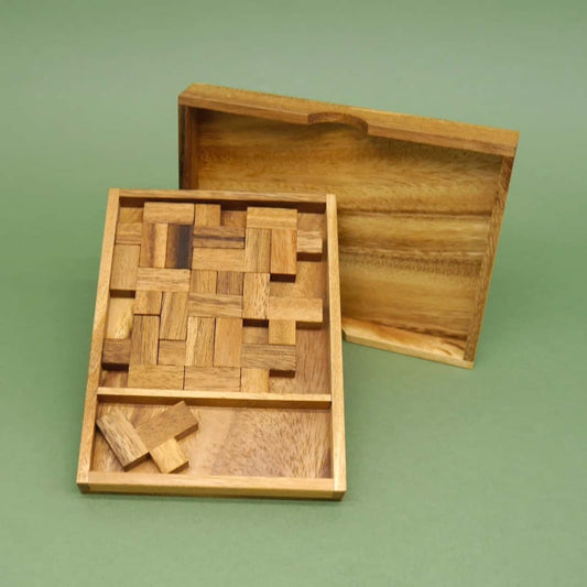 Gelöstes Packingpuzzle in einem Holzrahmen; der passende Deckel steht geöffnet dahinter.