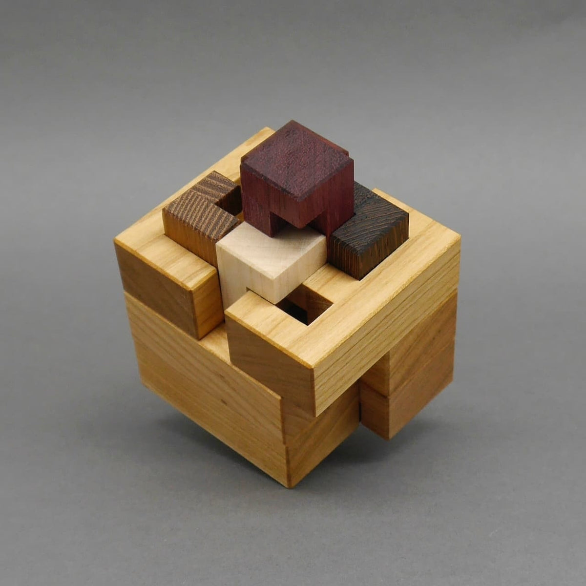 3D-Puzzle aus unterschiedlich gefärbten Holzklötzen, leicht geöffnet vor neutral grauem Hintergrund.