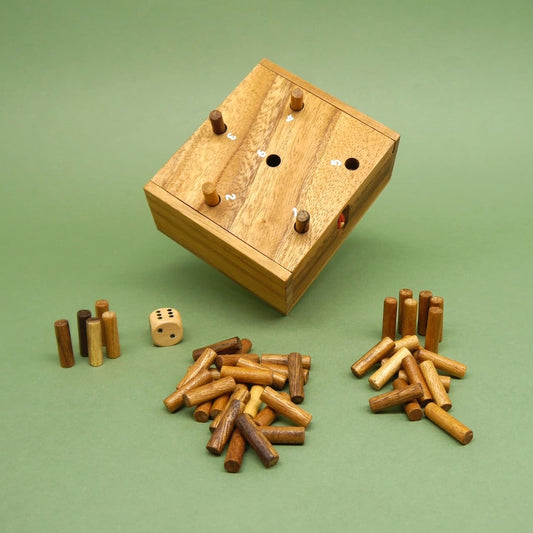 Schräg stehendes Kinderspiel aus Holz: Box mit nummerierten Löchern, ein Würfel sowie sortierte Holzstäbchenstapel davor.