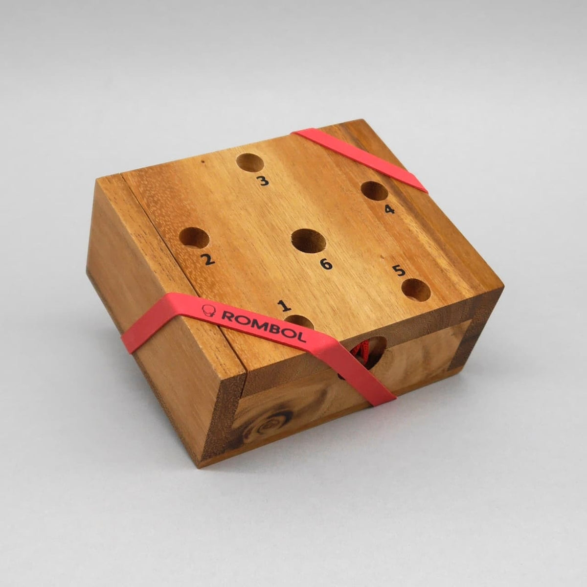 Geschlossenes Holz-Familienspiel mit nummerierten Löchern; rotes ROMBOL-Gummiband hält die Box zusammen.