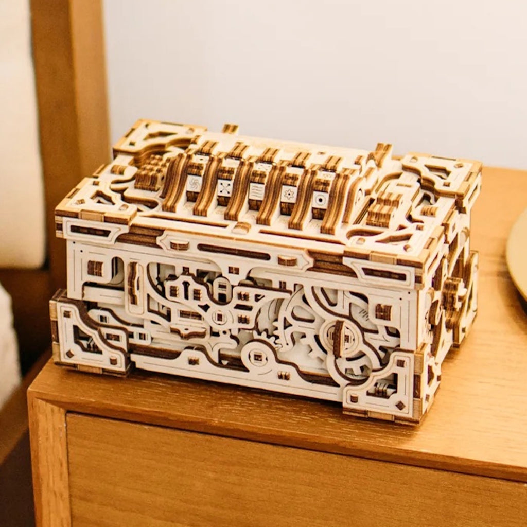Enigma Chest Designbox als Holzschachtel-Bausatz mit kunstvollen Zahnrädern und Zahlenschloss auf einem Holztisch.