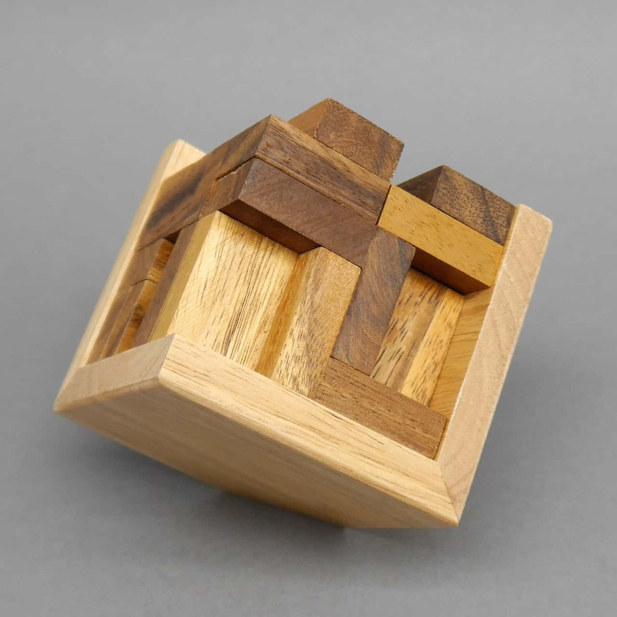 Schräg gekippter Holzquader zeigt ein verschachteltes Knobelspiel aus unterschiedlich dunklen Holzstücken.