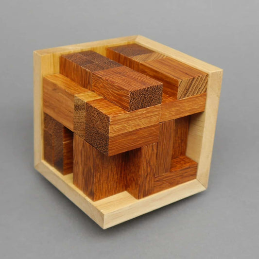 Ein vollständig zusammengesetztes Holz-Denkspiel zeigt eng verzahnte Quader in einer quadratischen Box vor grauem Hintergrund.