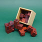 Aus einer gekippten Box purzeln mehrere ineinander gesteckte Holzwürfel‑Bausteine eines Holzpuzzles auf eine grüne Fläche.