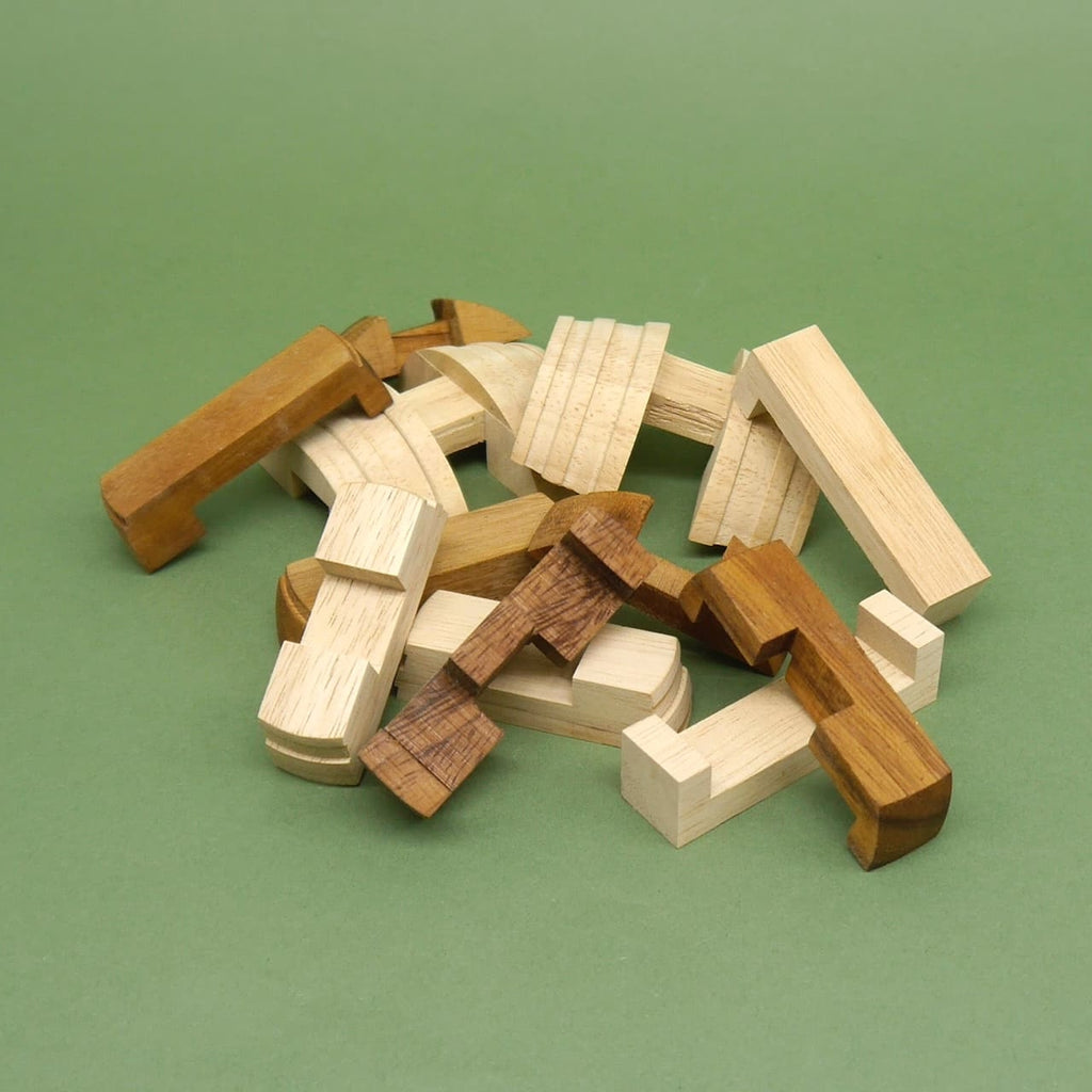 Lose verstreute Bausteine des „Fass des Diogenes“ Puzzle-Logikspiels: helle und dunkle Holzteile bilden das Denkspiel auf grüner Fläche.