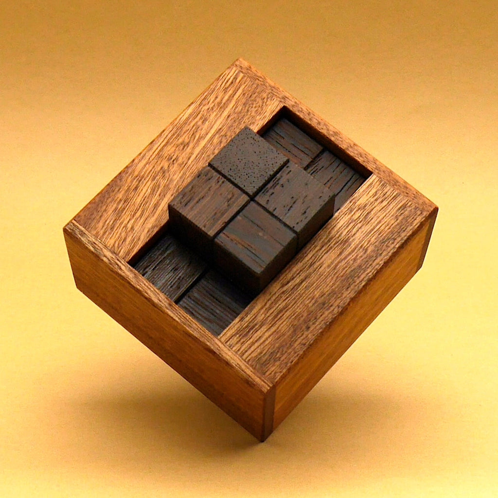 Puzzle aus dunklen Holzwürfeln in quadratischer Holzbox, von oben fotografiert – Denkspiel für Gehirnjogging.