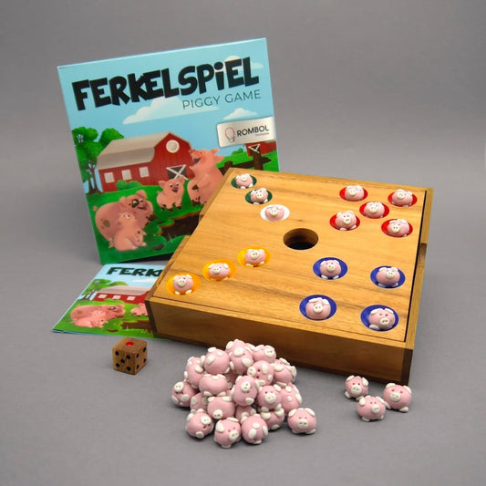 Aufgebautes Gesellschaftsspiel „Ferkelspiel“ mit Verpackung, Anleitung, Holzbrett mit farbigen Schweinchen-Steinen, Holzwürfel sowie Schweinchen-Haufen im Vordergrund.