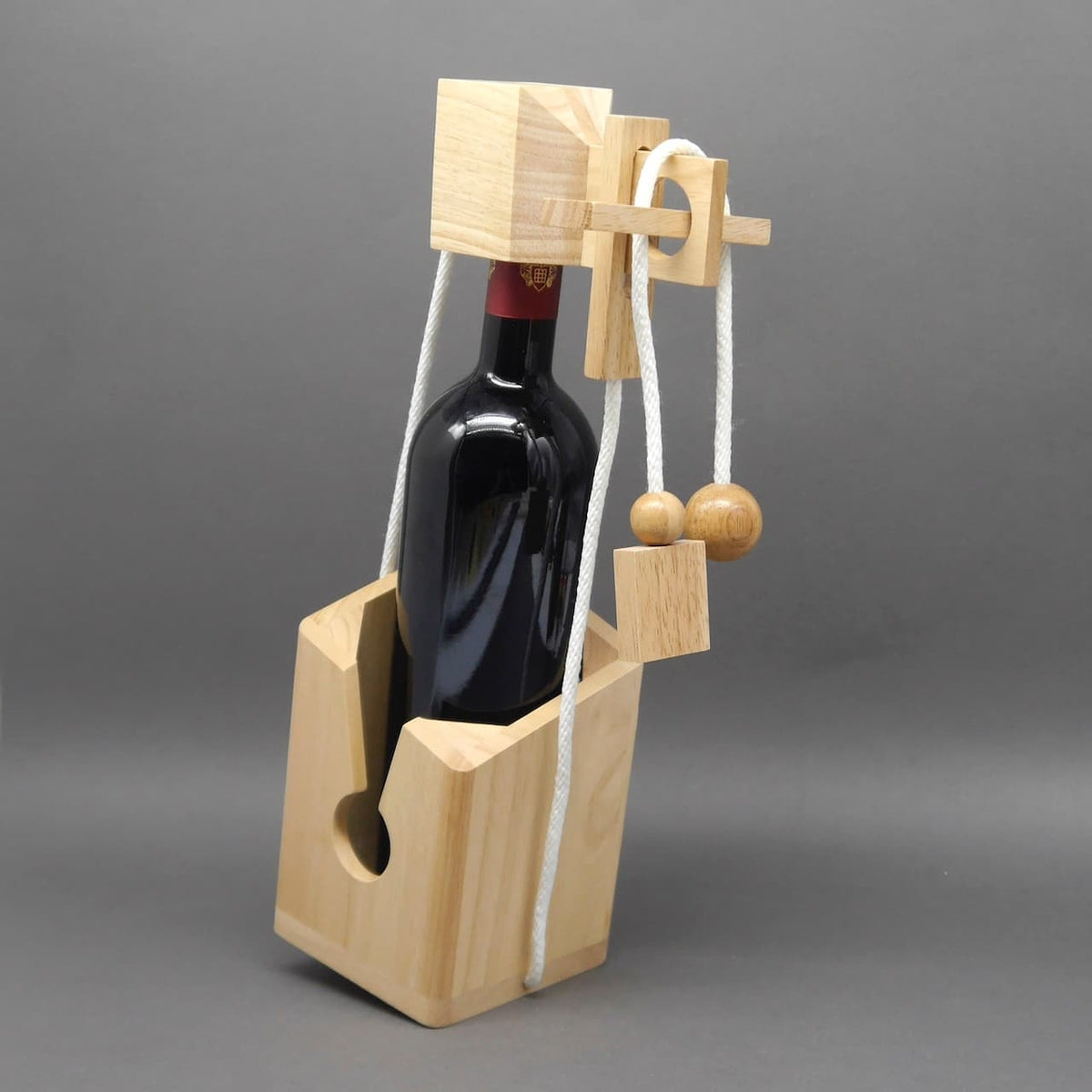 Geschenkverpackung für Wein aus Holz: Seil- und Kugel-Puzzle fixiert die Flasche in einem massiven Halter.