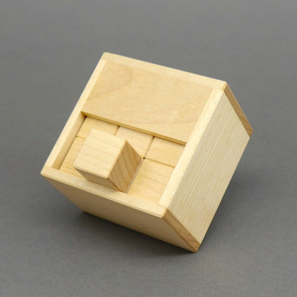 Geschlossenes Denkspiel aus Holz: alle Würfelmodule sind passgenau in einer Box verstaut, ein zentrales Teil ragt oben heraus.