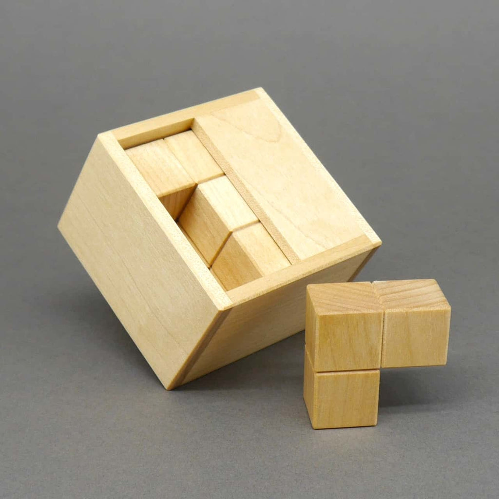 Teilgelöstes Logikspiel: schräg liegende Holzbox zeigt fast vollständig eingesetzte Würfelteile, ein letztes Element steht daneben.