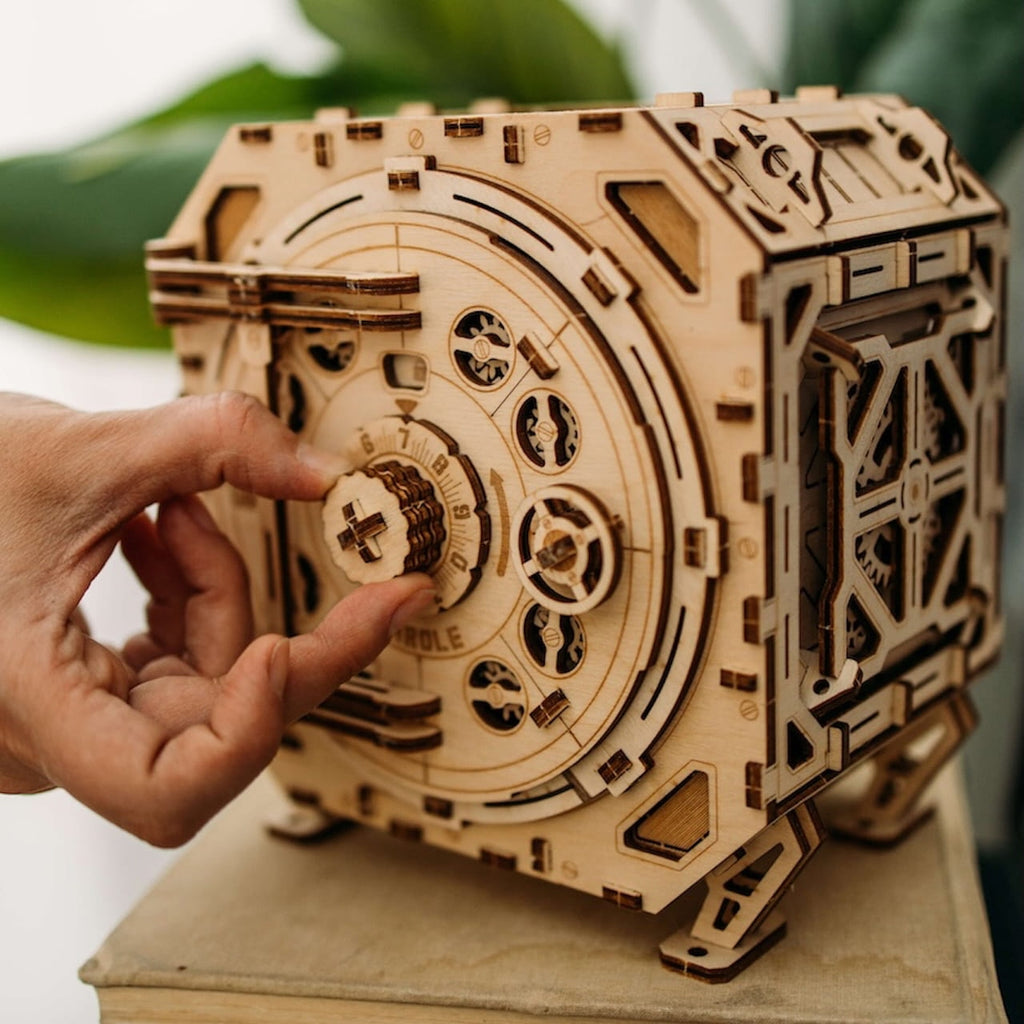Knobelspiel Geldtresor aus Holz, Hand dreht am Zahlenschloss der Konbelbox mit sichtbaren Zahnrädern.