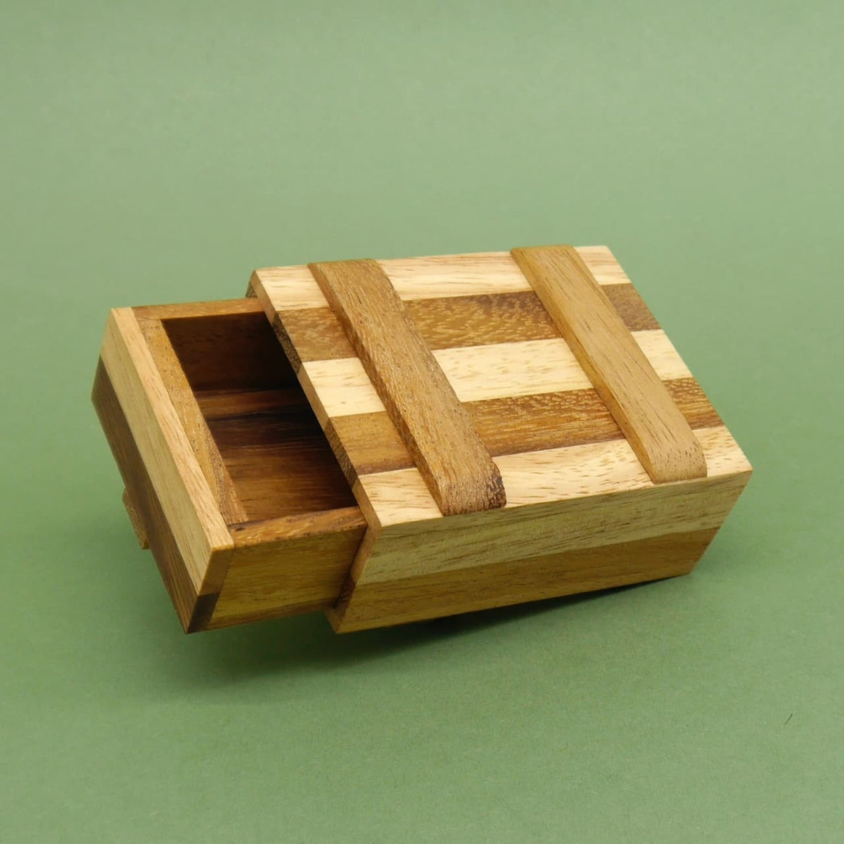 Kleine Schatztruhe aus Holz mit seitlich herausgezogenem Fach vor einfarbig grünem Untergrund.