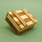 Geschlossene Woodenbox mit hell‑dunklen Holzstreifen, schräg liegend auf grünem Hintergrund.