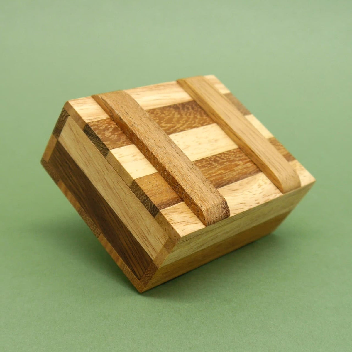 Geschlossene Woodenbox mit hell‑dunklen Holzstreifen, schräg liegend auf grünem Hintergrund.