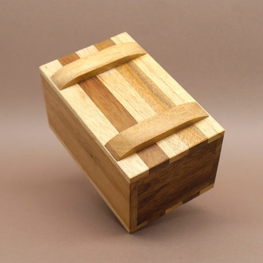 Zweifarbig gestreifte Holzbox aus Massivholz, leicht geneigt aufgestellt – eine dekorative Knobelbox.