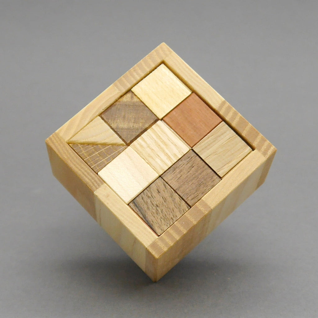 Giro Packpuzzle von oben: quadratische Holzbox mit bereits eingelegten dreieckigen Teilen in Braun- und Holztönen.