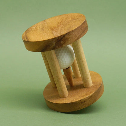 Schräg gekipptes Denkspiel‑Puzzle aus Holz, in dessen Mitte ein weißer Golfball auf einem Tee zwischen den Stäben steckt.