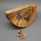 Ein zusammenklappbares Halma-Brettspiel aus Holz. Die Spielfiguren sind teilweise auf dem Brett platziert, während weitere Holzfiguren lose davor liegen. Das Brett zeigt Scharniere für die Klappfunktion, wodurch es leicht zu transportieren und aufzubewahre