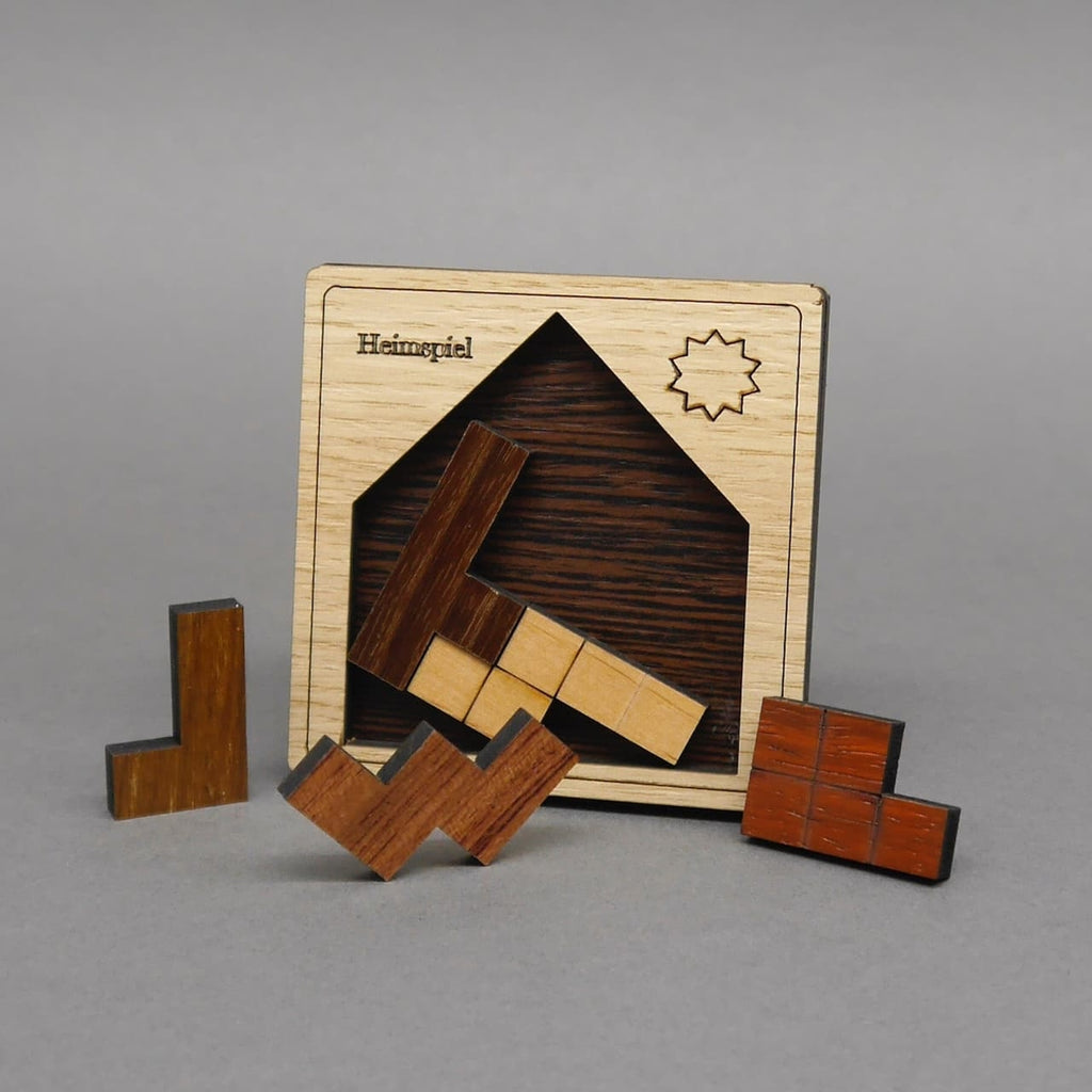 Aufrecht stehendes Holzpuzzle „Heimspiel“ mit Sonnengravur; leerer Hausrahmen, fünf verschiedenfarbige Holzsteine sind davor verteilt.