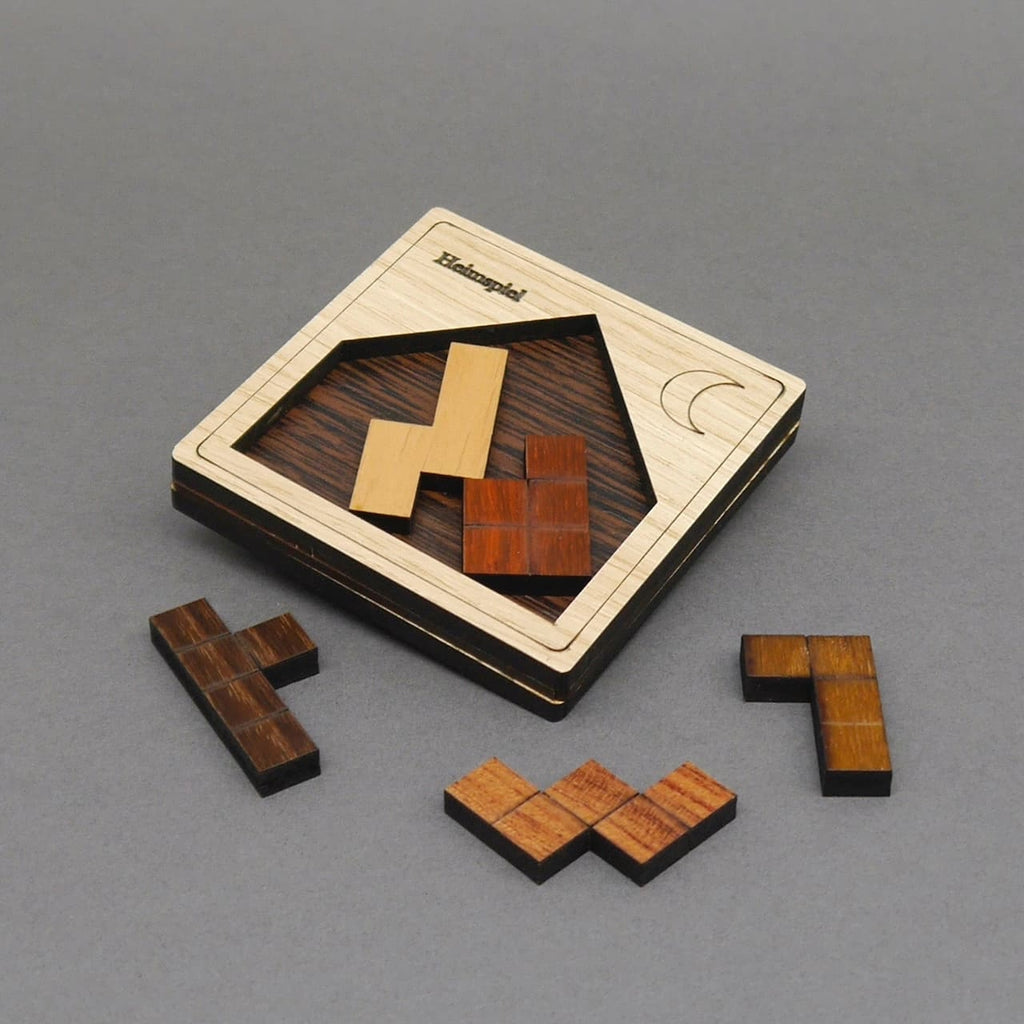Schräg liegendes Holzpuzzle „Heimspiel“ mit Mondgravur; zwei Steine eingesetzt, vier braune und ockerfarbene Tetrisformen liegen drumherum.