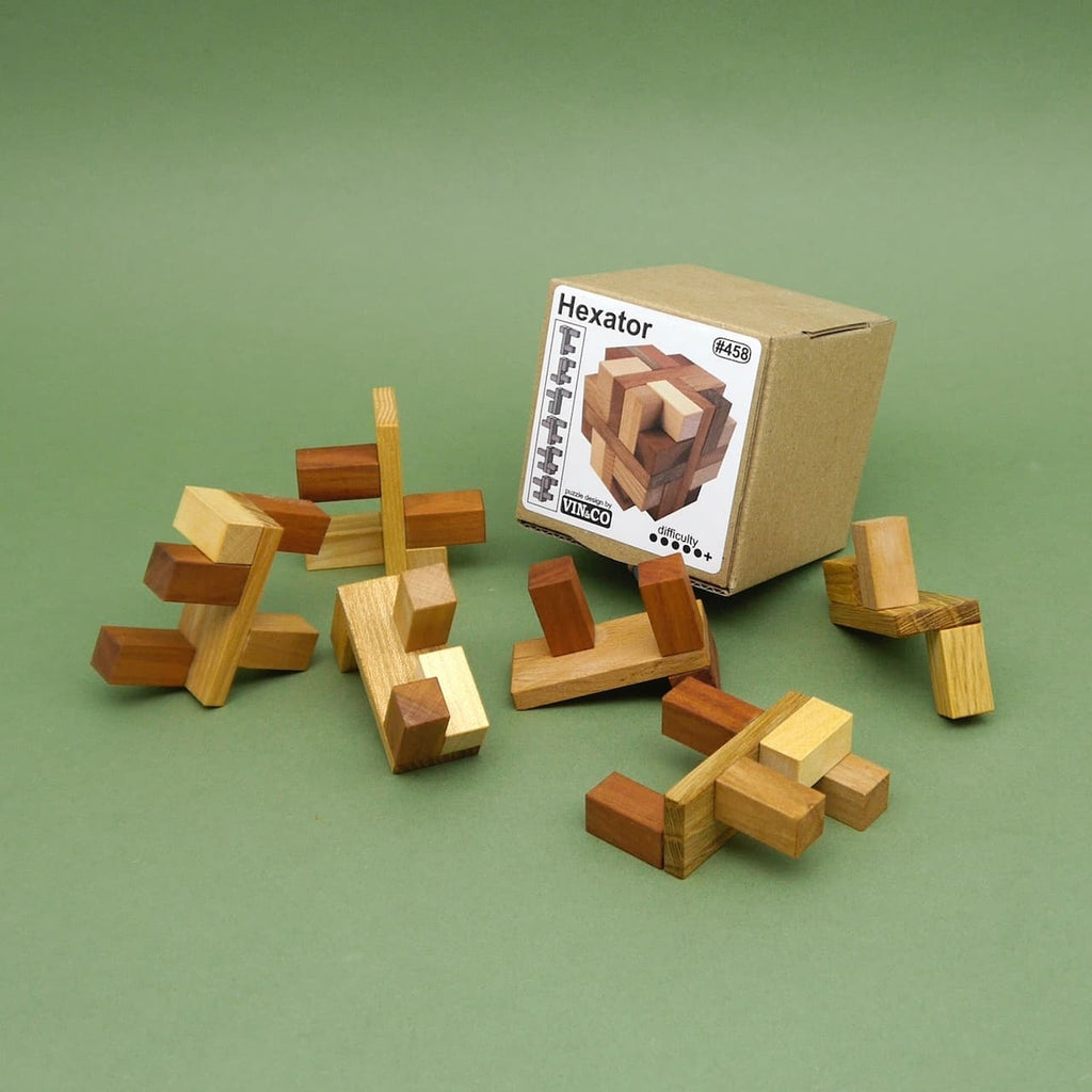 Einzelne Holzteile des Hexator Gehirntraining-Puzzles liegen vor einer Kartonbox mit Produktetikett auf grünem Untergrund.