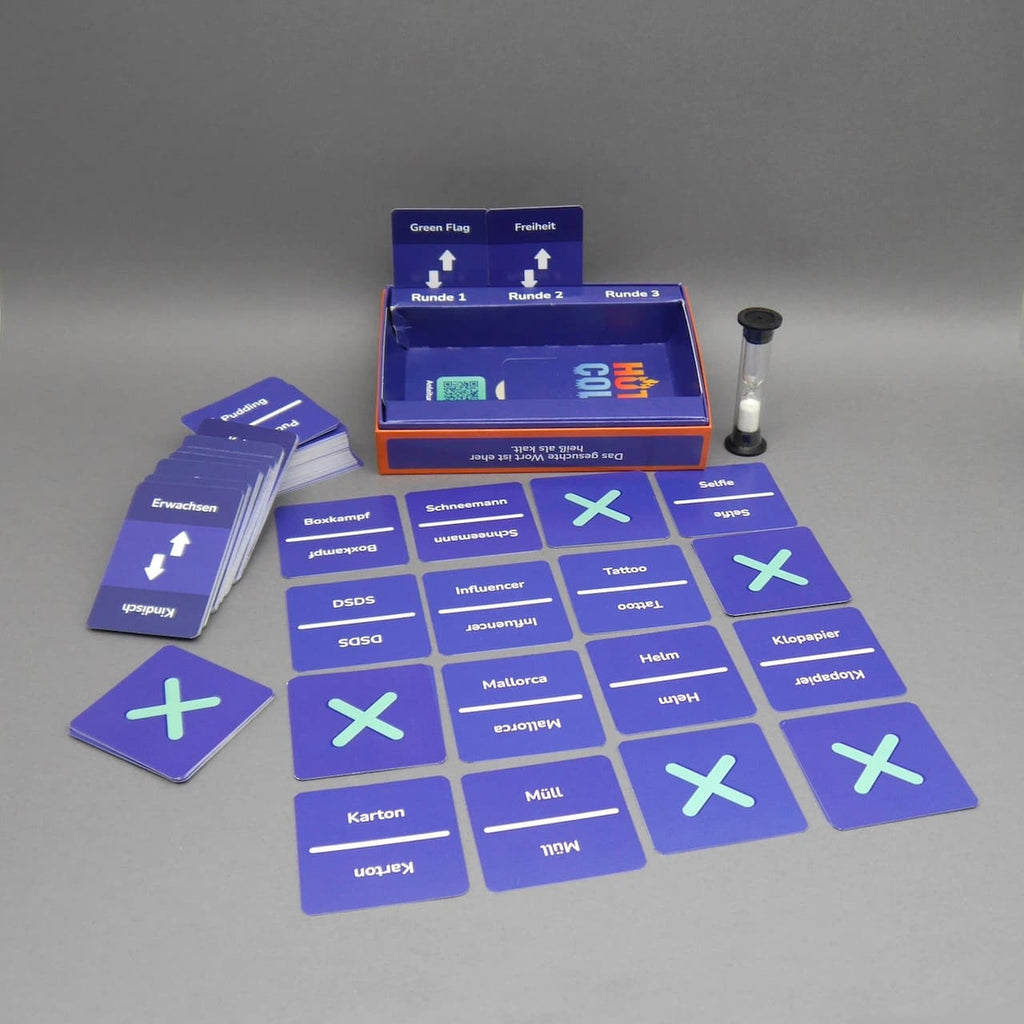 Geöffnete „Hot or Cold“-Box mit Sanduhr und in einem Raster ausgelegten Karten – bereit für eine Runde.