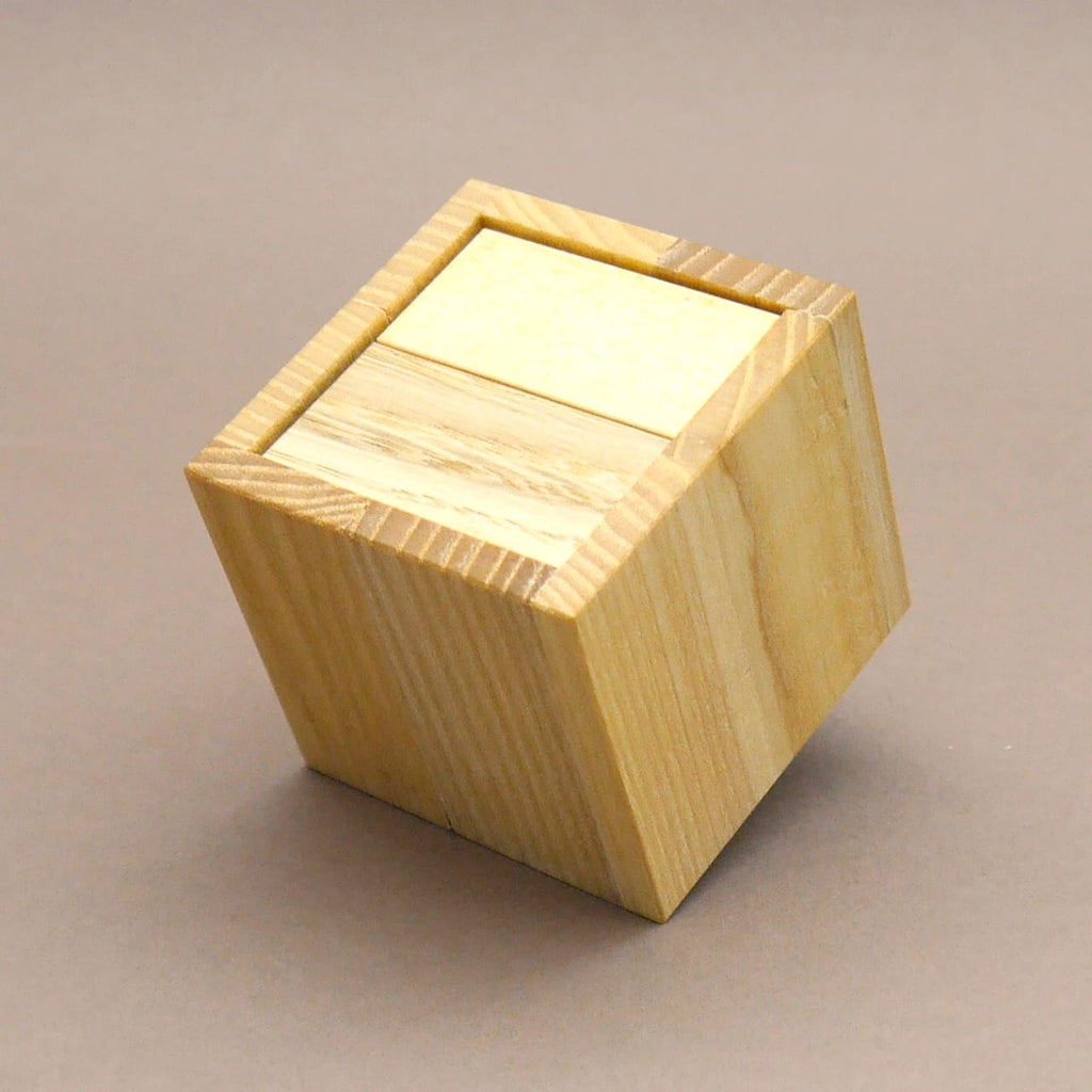 Schräg stehender Holzwürfel eines Holzpuzzle mit eingelassenem Deckel auf neutralem Hintergrund.