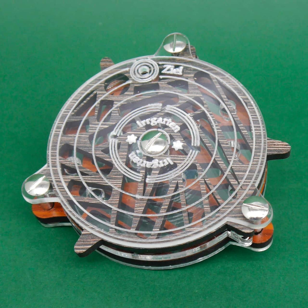 Oberansicht eines runden Labyrinth-Puzzles aus Holz und Acryl, mit der Gravur ‚Irrgarten‘ auf dem transparenten Deckel, vor grünem Hintergrund.