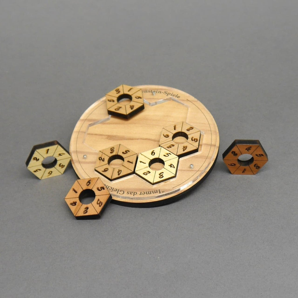 Ein rundes Holzpuzzle mit vertieften Aussparungen; einige nummerierte Sechseckringe sind bereits eingelegt, andere liegen um die Scheibe herum.