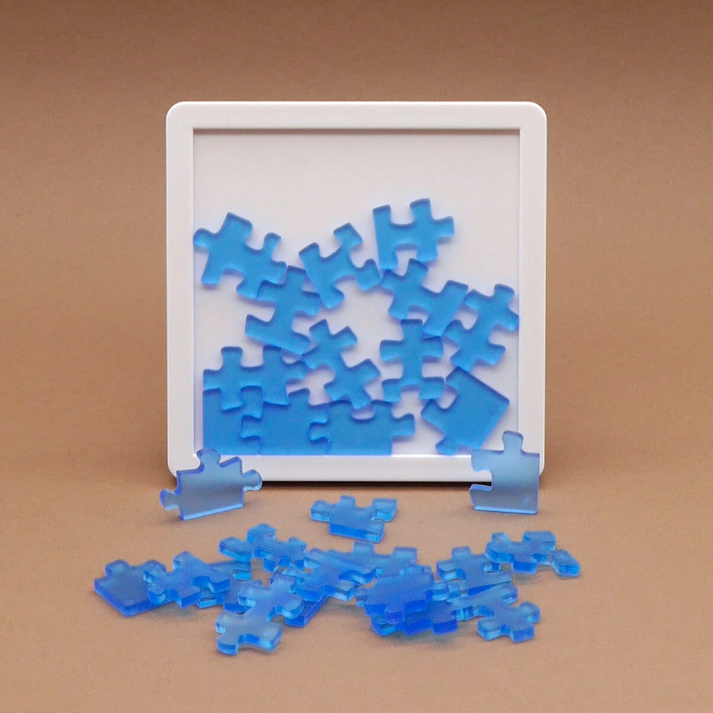 Denkspiele: Transparente blaue Puzzleteile liegen in weißem Rahmen und fördern Konzentration sowie räumliches Denken.