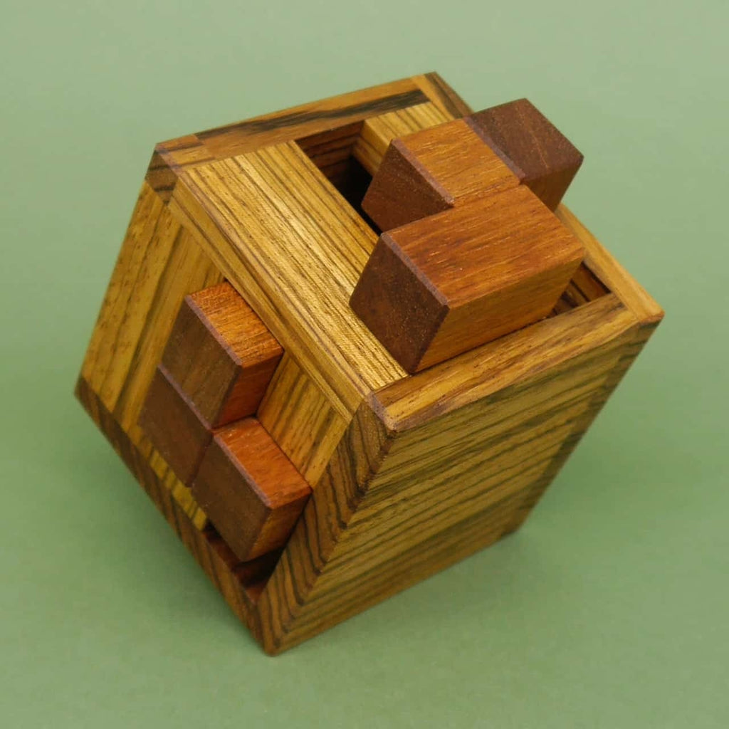 Geschlossener Holzwürfel als 3D-Puzzle, einzelne dunkle Holzsteine ragen heraus, vor einfarbig grünem Hintergrund.