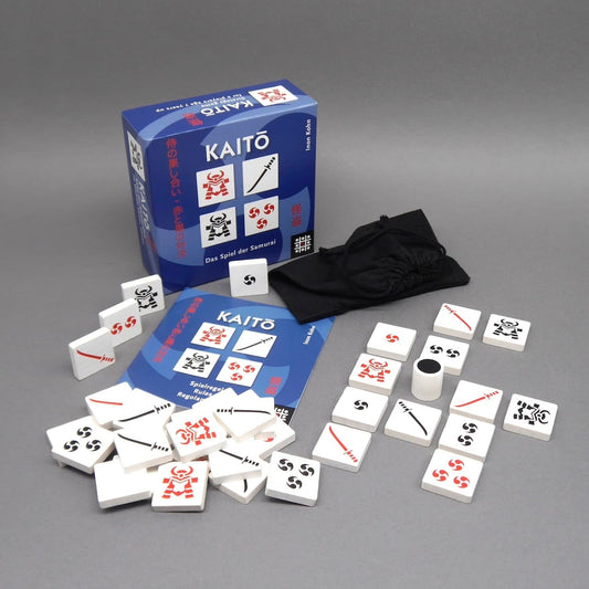 Das Gesellschaftsspiel Kaito für 2 Personen mit Spielsteinen, Anleitung, Würfel und Stoffbeutel – ausgelegt vor der Verpackung.