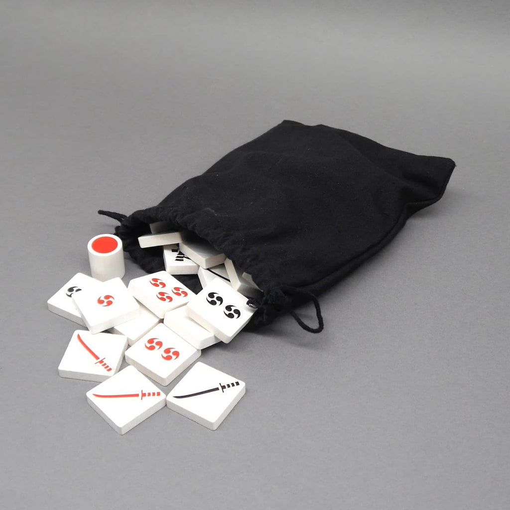 Ein schwarzer Beutel mit herausfallenden Spielsteinen und Würfel aus dem Taktikspiel Kaito, ideal als Kinderspiel und Familienspiel.