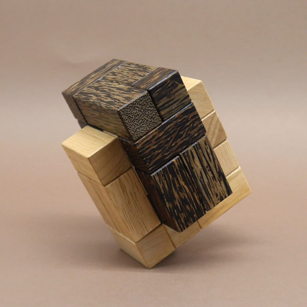 Holzpuzzle aus hellen und dunklen Quadern, zu einem komplexen Würfel zusammengesetzt und schräg auf einer Ecke balancierend.