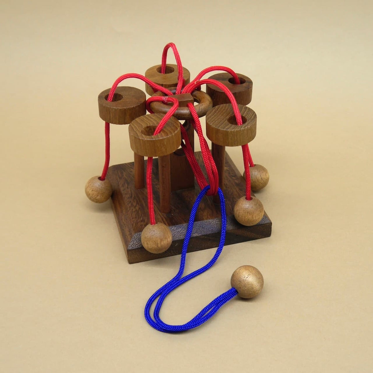 Komplexes Karusselpuzzle aus Holz mit roten und blauen Seilen als Geduldspiel.
